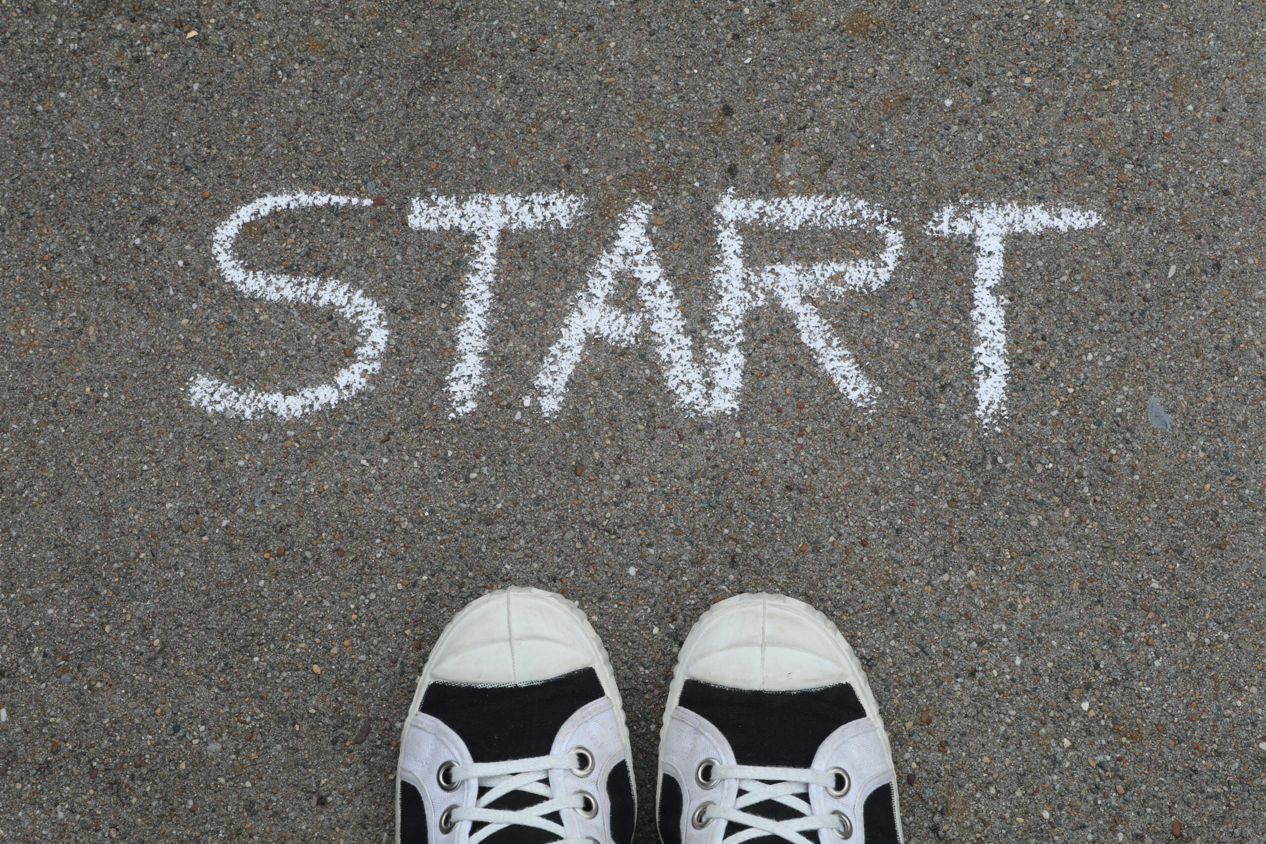 Close up of sneakers and a START chalk drawing on pavement symbolizing new beginnings
